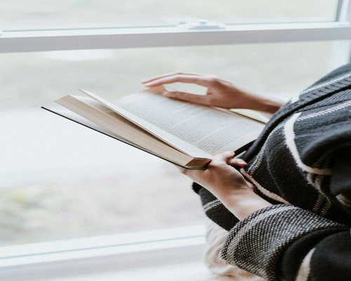 A person reading a book near a large window with natural light